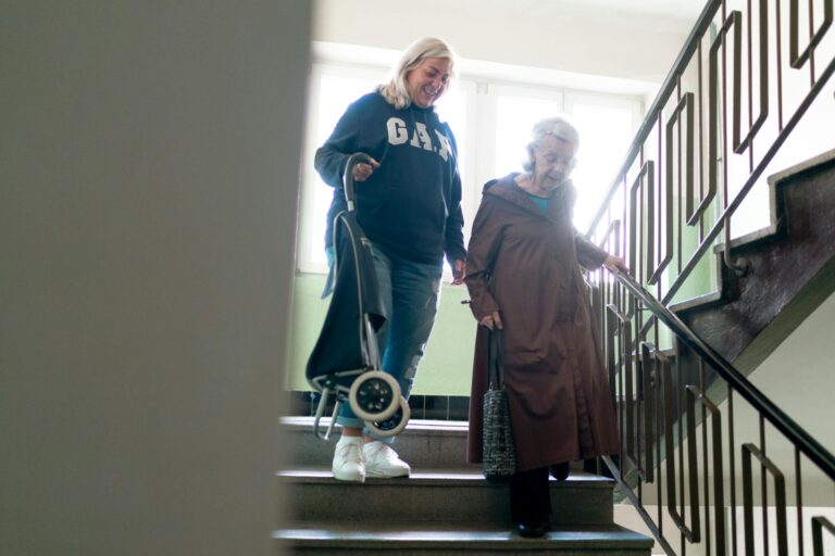 Caregiver helps senior woman navigate stairs indoors, emphasizing elderly care and support.